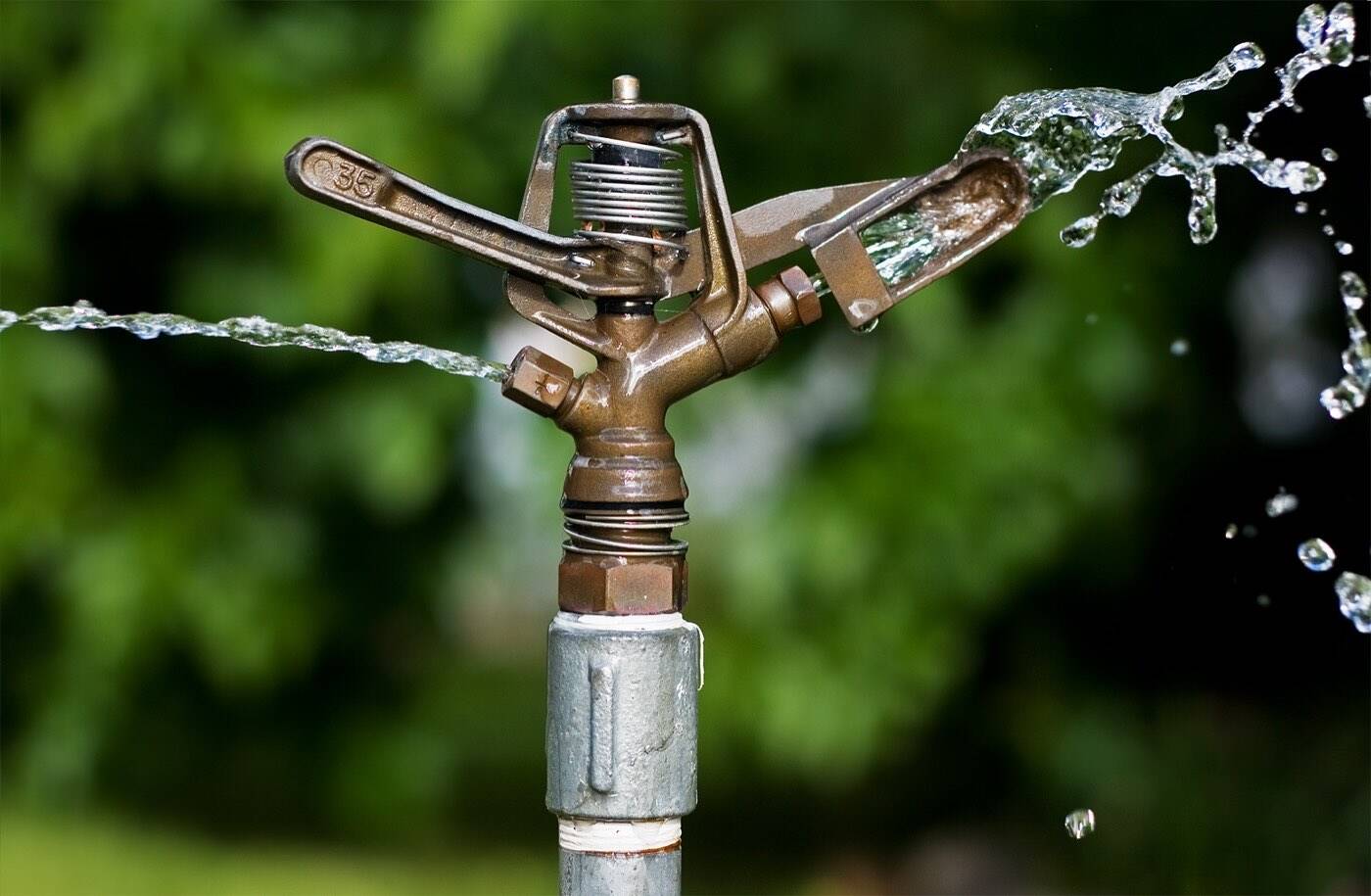 Nahaufnahme eines Impuls-Regners aus Metall, der Wasserstrahlen über den Garten verteilt